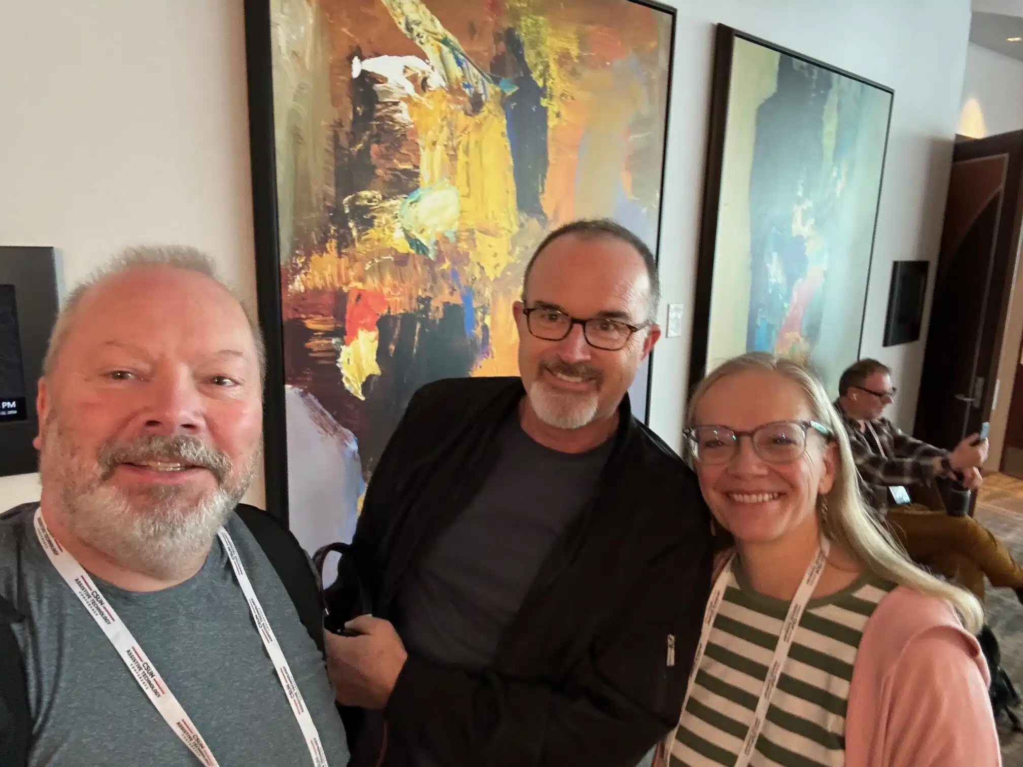 Three participants at CSUN conference. Two white, middle-aged men with shaved haircuts and goatee beards. A middle-aged white woman with long silver hair.