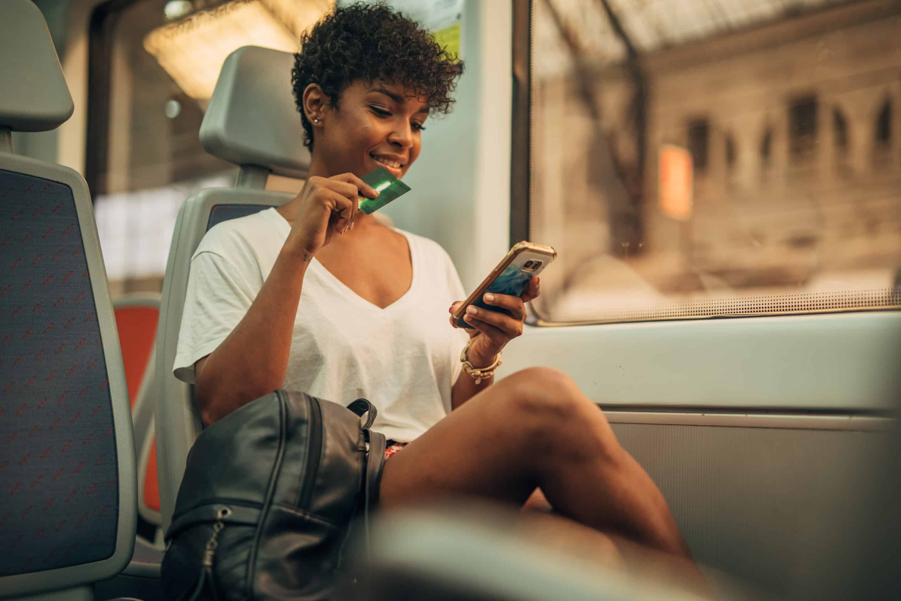 GettyImages-1198608401-scaled-1 Woman on a train making a transaction with credit card