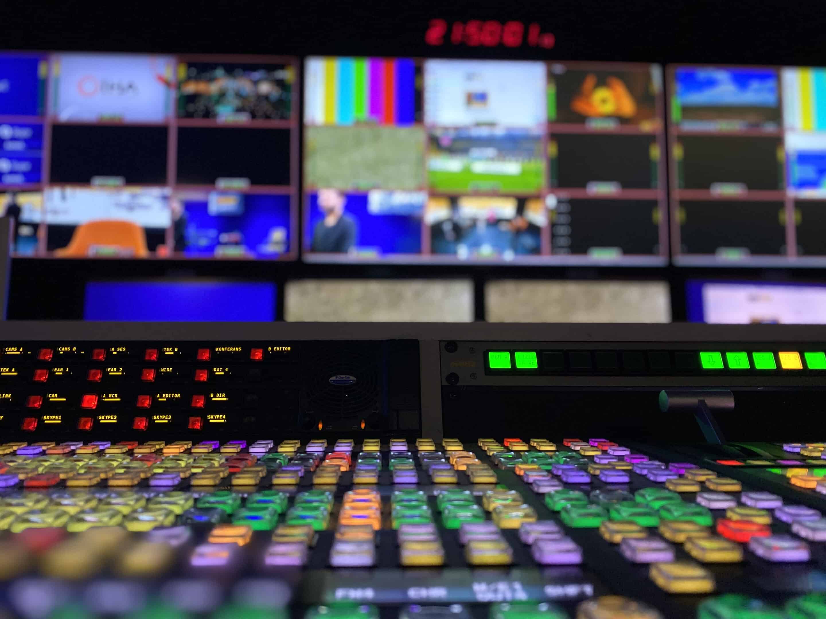 Rows of buttons in a TV media center in front of a wall of TV screens.