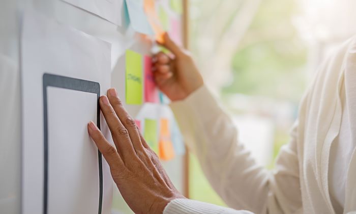 A close up of hands on a whiteboard surorunded by colorful post-its as a UX researcher makes note on how to design an app based on user feedback.