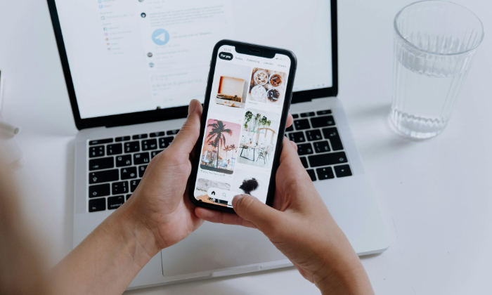 MKT7026-user-phone A person holds a phone while also using a laptop.