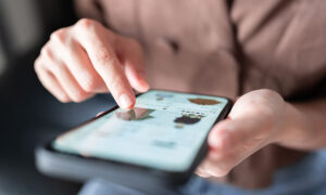 Closeup of a Caucasian woman's hand shopping for clothing on a mobile phone.