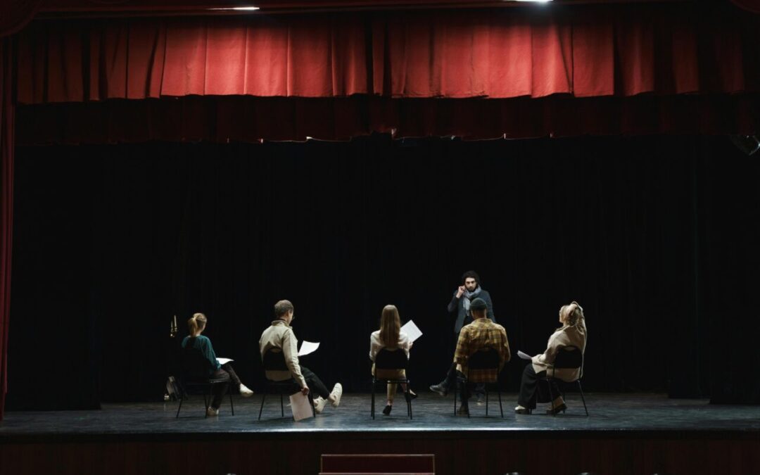 Performers sit and read scripts on a stage.