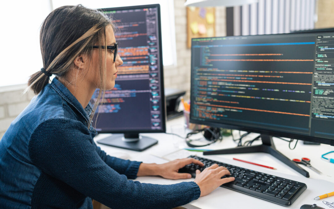 A woman works on two computer screens with code.