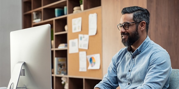 A man wearing glasses sitting in his office working at his computer.