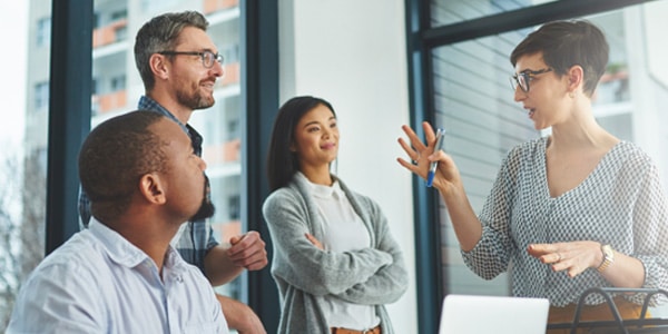 Woman holding a pen talking to coworkers in a sunny office.