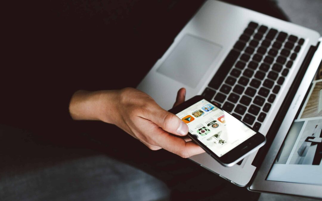 A close-up of a hand holding a mobile phone appears slightly above an laptop.