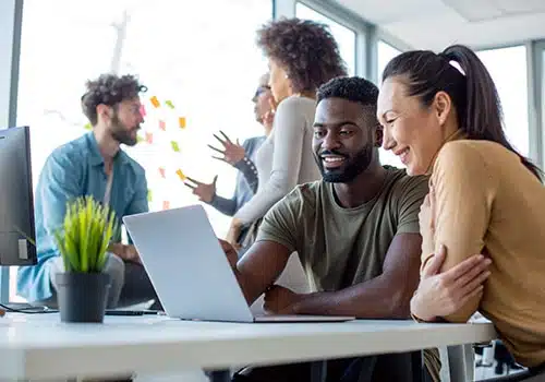 Two people view a screen while others engage in a conversation behind them.