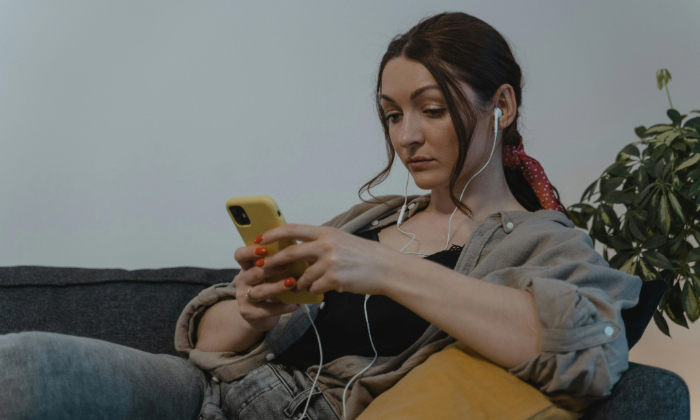 A woman wearing wired ear buds watches a video on her phone.