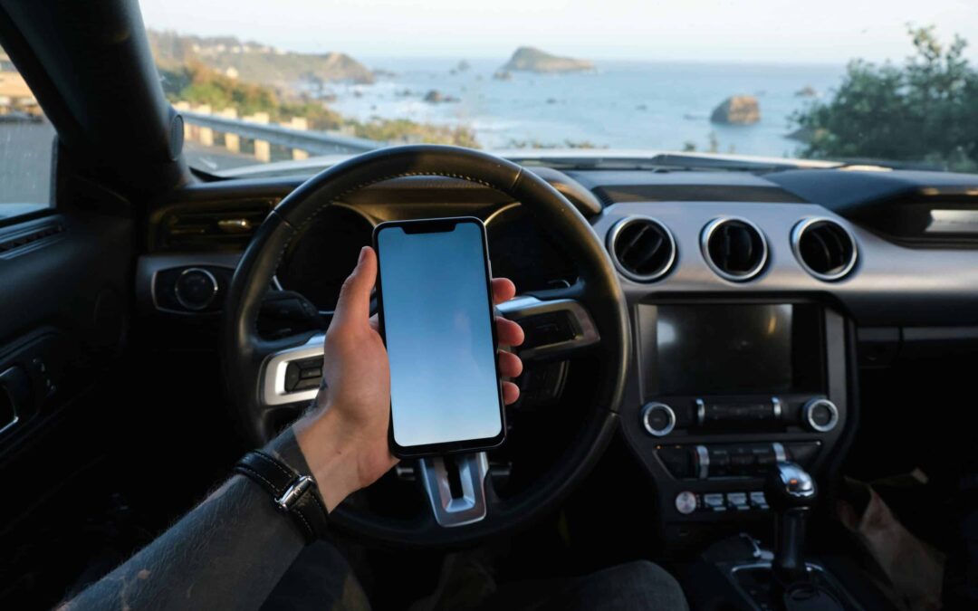 A driver looks at a mobile phone while sitting parked in a car overlooking the water.