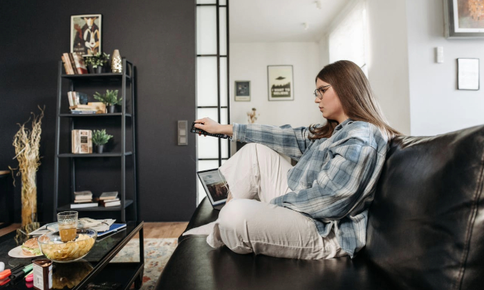 A woman sits on a couch pointing a remote at a TV.