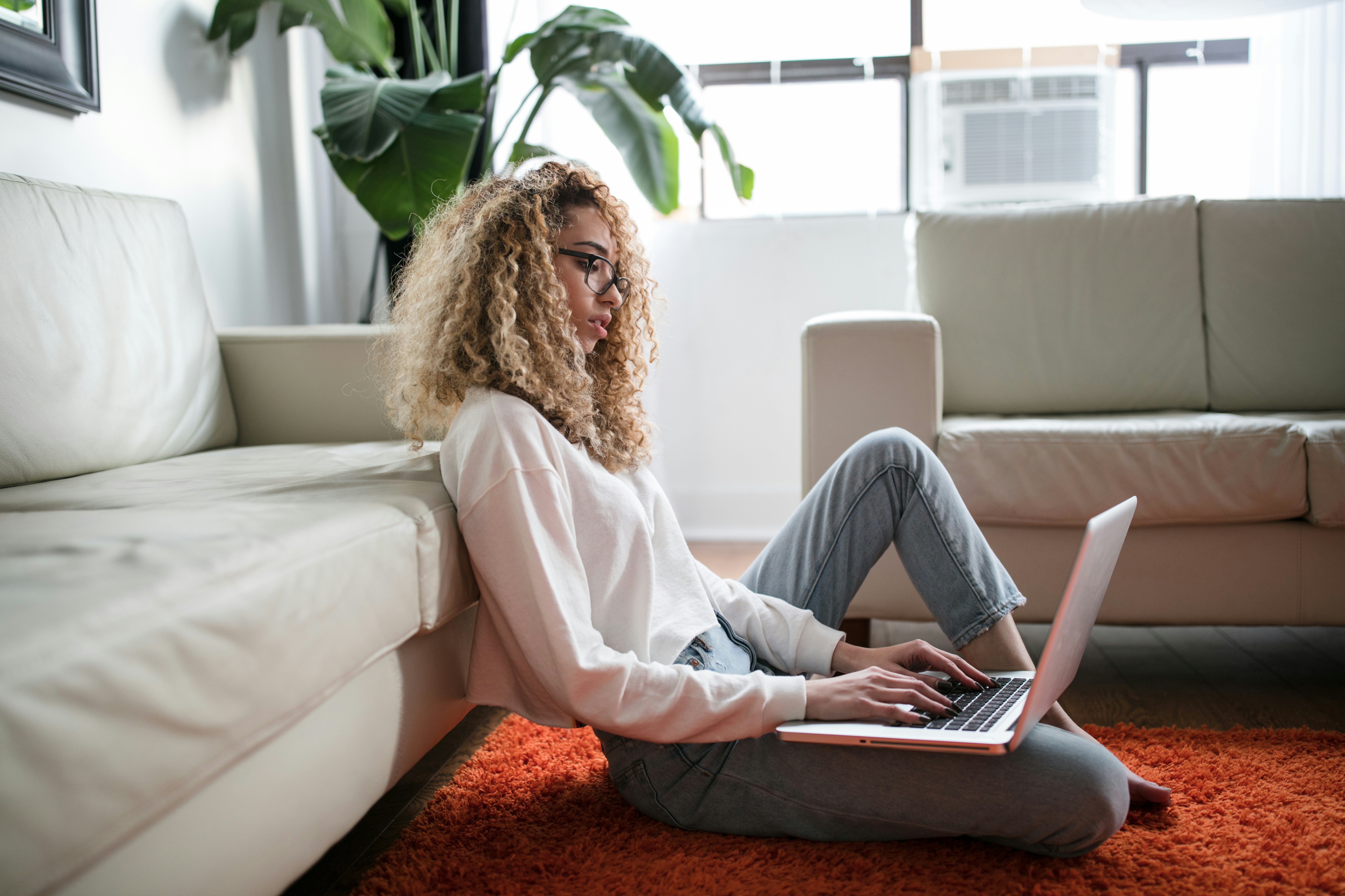 Woman sits on the floor with her laptop in her lap.