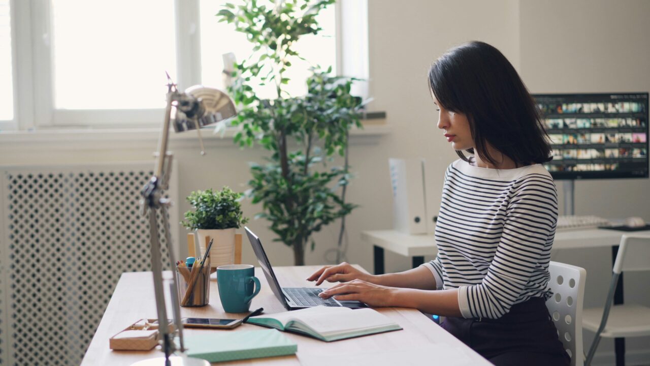vitaly-gariev-1ZrHX1Kj594-unsplash-scaled-1 A woman sits at her desk typing on her laptop.